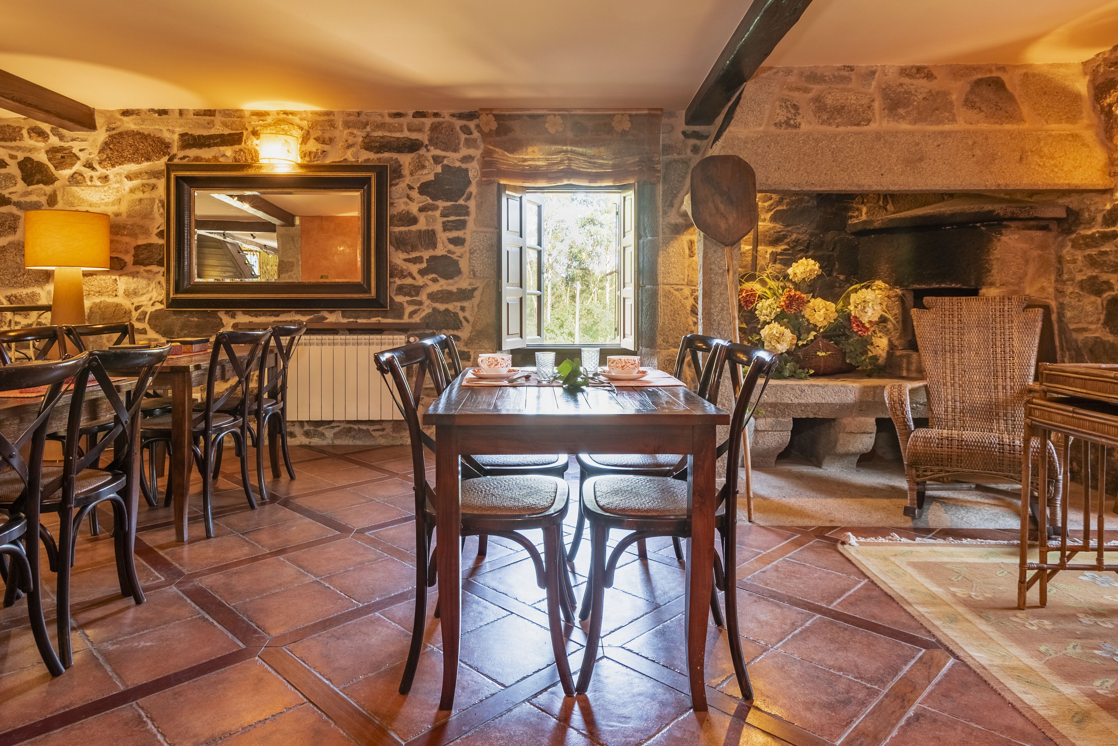 Uma sala de jantar com paredes de pedra, uma mesa grande e cadeiras, uma lareira e uma janela com vista.