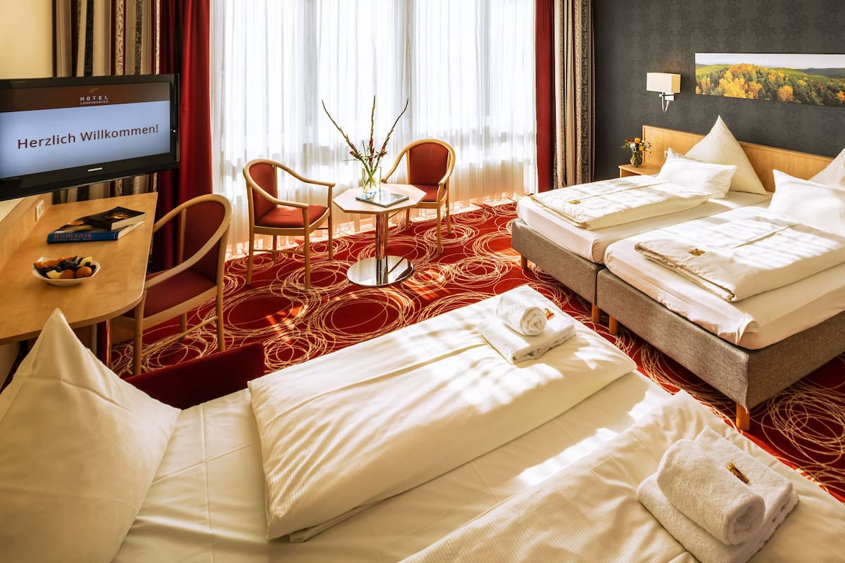 A hotel room with two beds, a desk, a chair, a TV displaying a welcome message, and a painting on the wall.