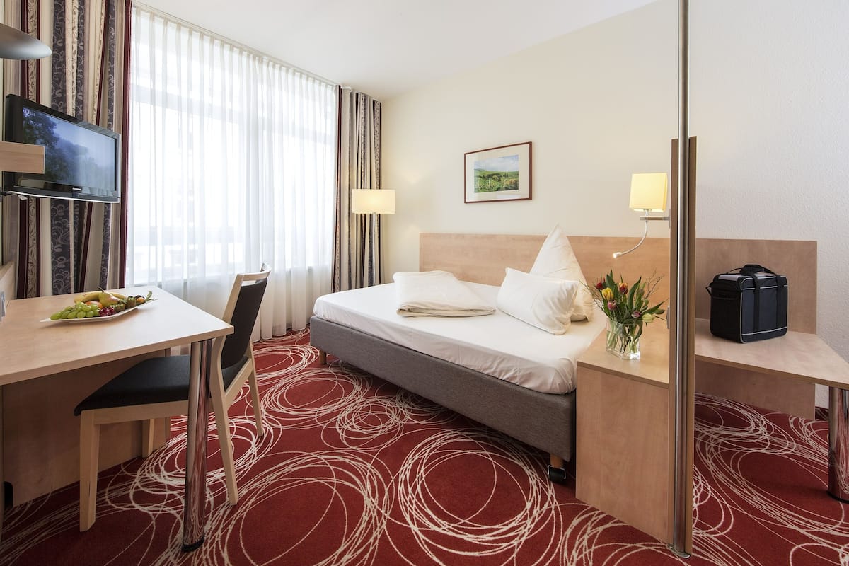 A hotel room with a bed, desk, chair, TV, and a small table with fruit.