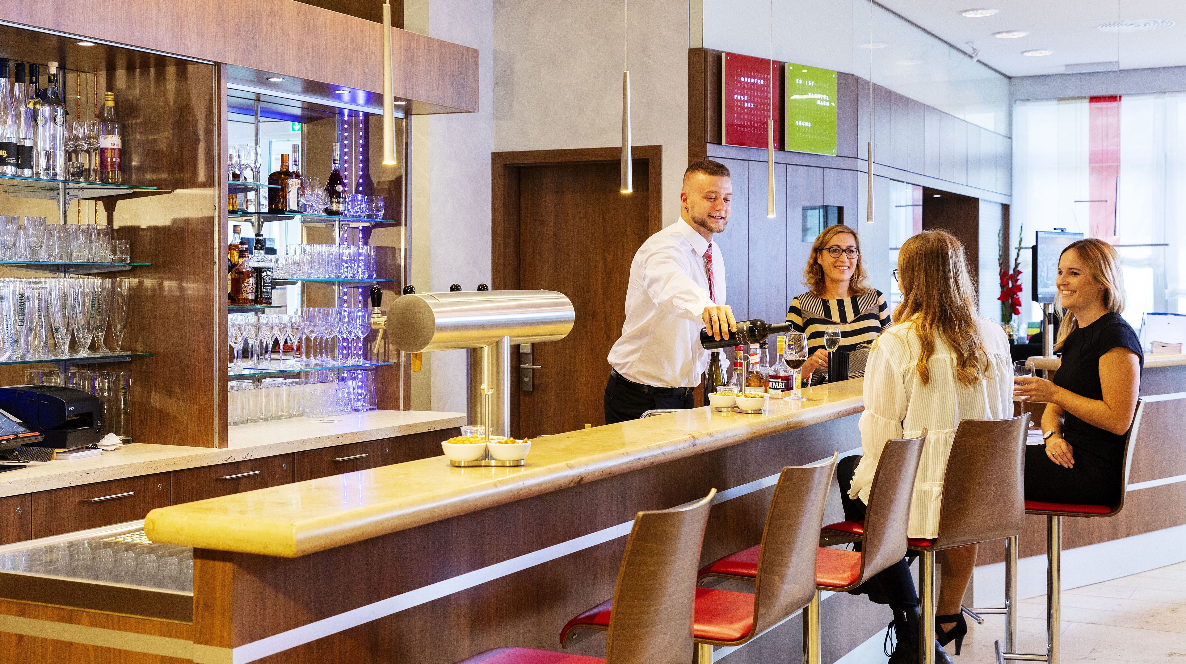 Een bar met een barman die drankjes klaarmaakt, een kassa en een wijnkoeler.