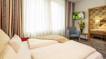 A hotel room with a bed, a chair, a TV, and a vase with flowers.