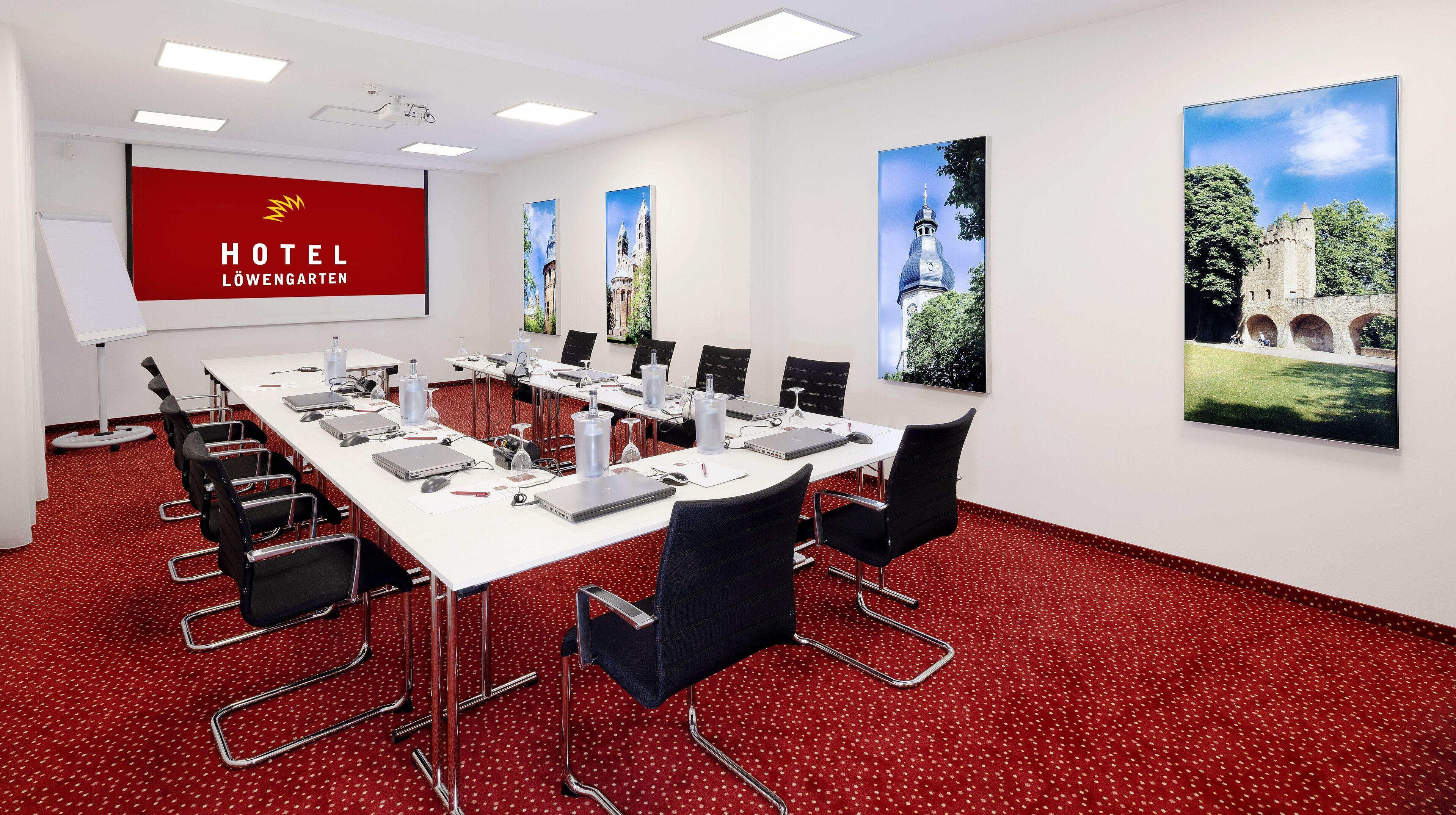 Un salón de conferencias de hotel con alfombra roja, mesas blancas y sillas negras.