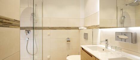 Un baño moderno con ducha de vidrio, inodoro y tocador con lavamanos y espejo.