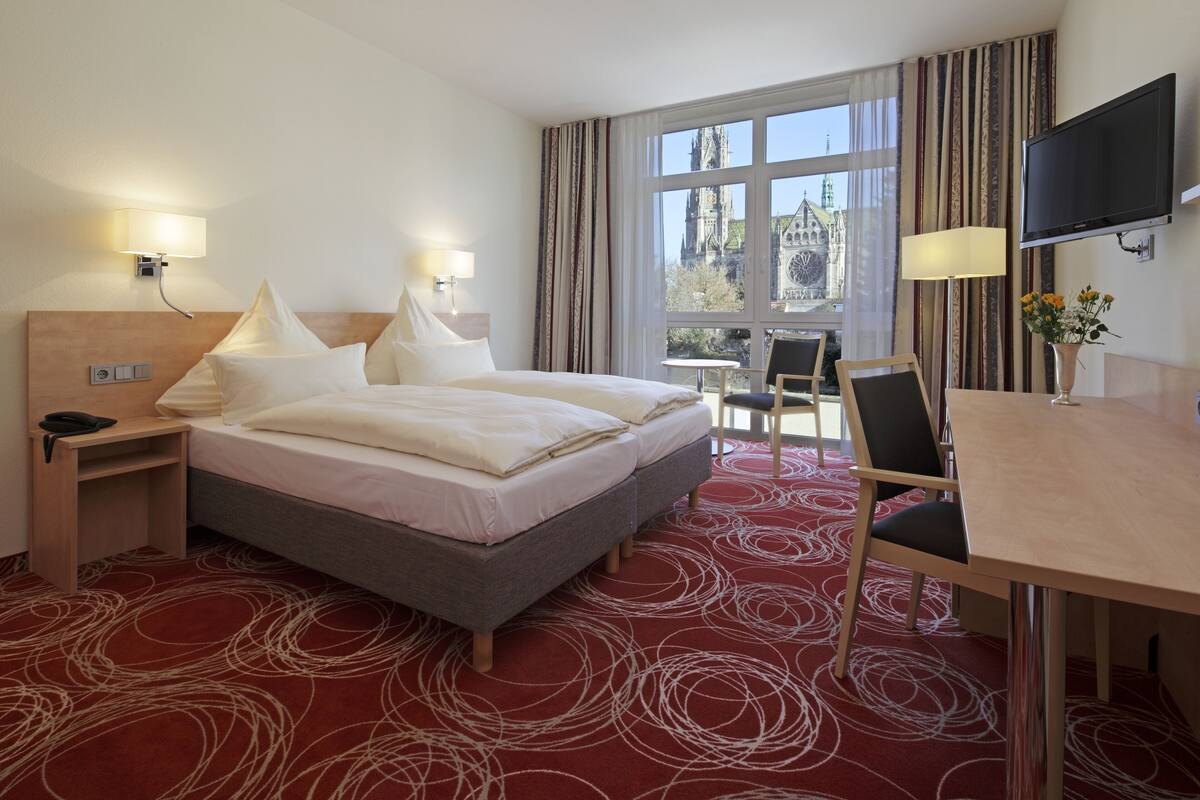 A hotel room with a large bed, a desk, a chair, and a TV.