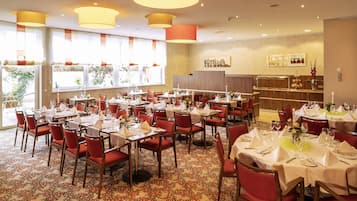 Un restaurante con varias mesas dispuestas para comer, sillas rojas y una alfombra estampada.