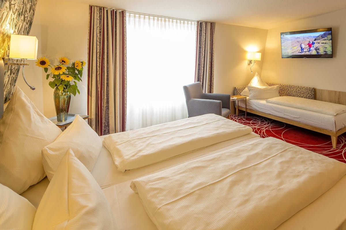 A hotel room with a bed, a chair, a TV, and a shower area.