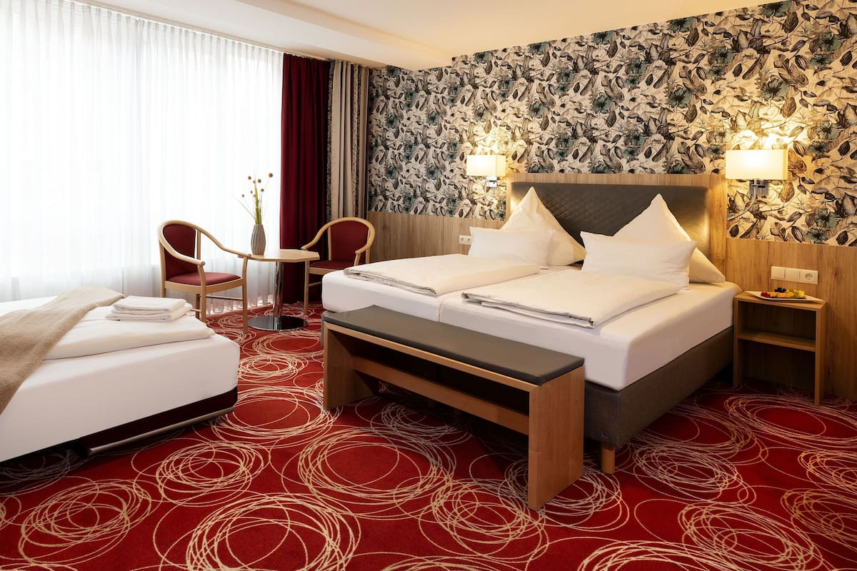 A hotel room with a bed, a desk, a chair, and a wall with floral wallpaper.