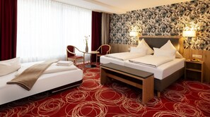 A hotel room with a bed, a desk, a chair, and a wall with floral wallpaper. - Hotel Löwengarten (Speyer)