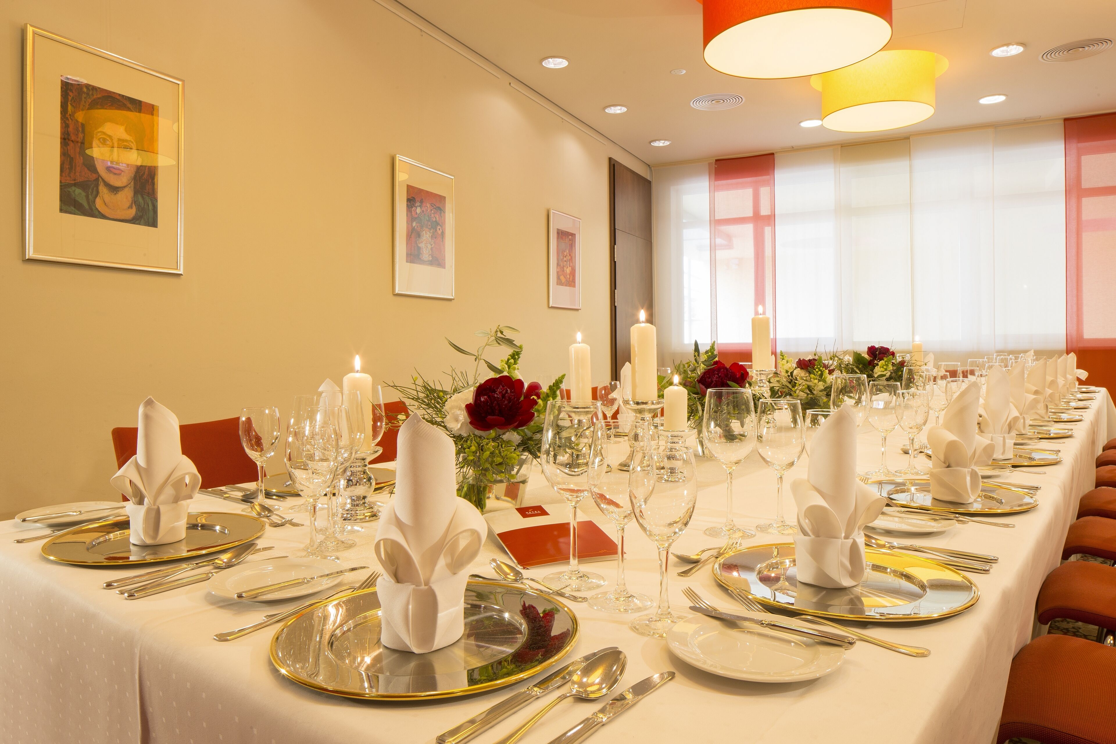 Una larga mesa de comedor dispuesta para una comida formal, con múltiples puestos, velas y centros de mesa con flores.