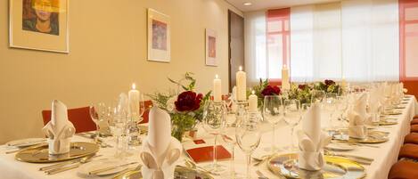 Una larga mesa de comedor dispuesta para una comida formal, con múltiples puestos, velas y centros de mesa con flores.