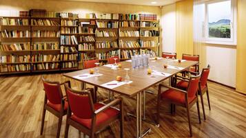A conference room with a wooden table, red chairs, and a bookshelf filled with books.