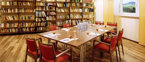 Una sala de conferencias con una mesa de madera, sillas rojas y una estantería llena de libros.