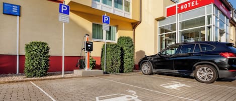 A hotel with a parking area, electric vehicle charging station, and a black car parked.