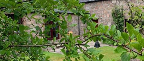 A stone building with a grassy yard and a tree in the foreground.
