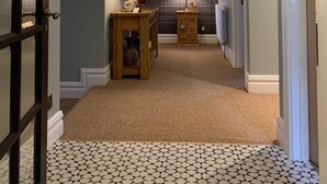 Un couloir avec un tapis à motifs, une horloge au mur et deux tables avec des lampes.