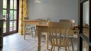 Un coin repas avec une table et des chaises en bois, un ventilateur de plafond et une vue à travers une porte vitrée.