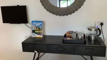 Habitación de hotel con escritorio, televisión, espejo, un libro, cafetera y cama con cubrecama estampado.