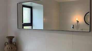 Une salle de bain avec un grand miroir, un vase et une baignoire.