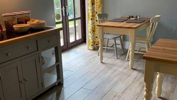 A kitchen with a wooden table and chairs, a cabinet with drawers, a window with curtains, and a door leading outside.