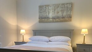 Une chambre à coucher avec un lit, deux tables de chevet avec des lampes, une commode, un tableau accroché au mur et un plancher en bois.