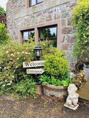 Un edificio de piedra con un cartel que dice 'Welcome Entrance', rodeado de abundante vegetación y una estatua decorativa de un león.
