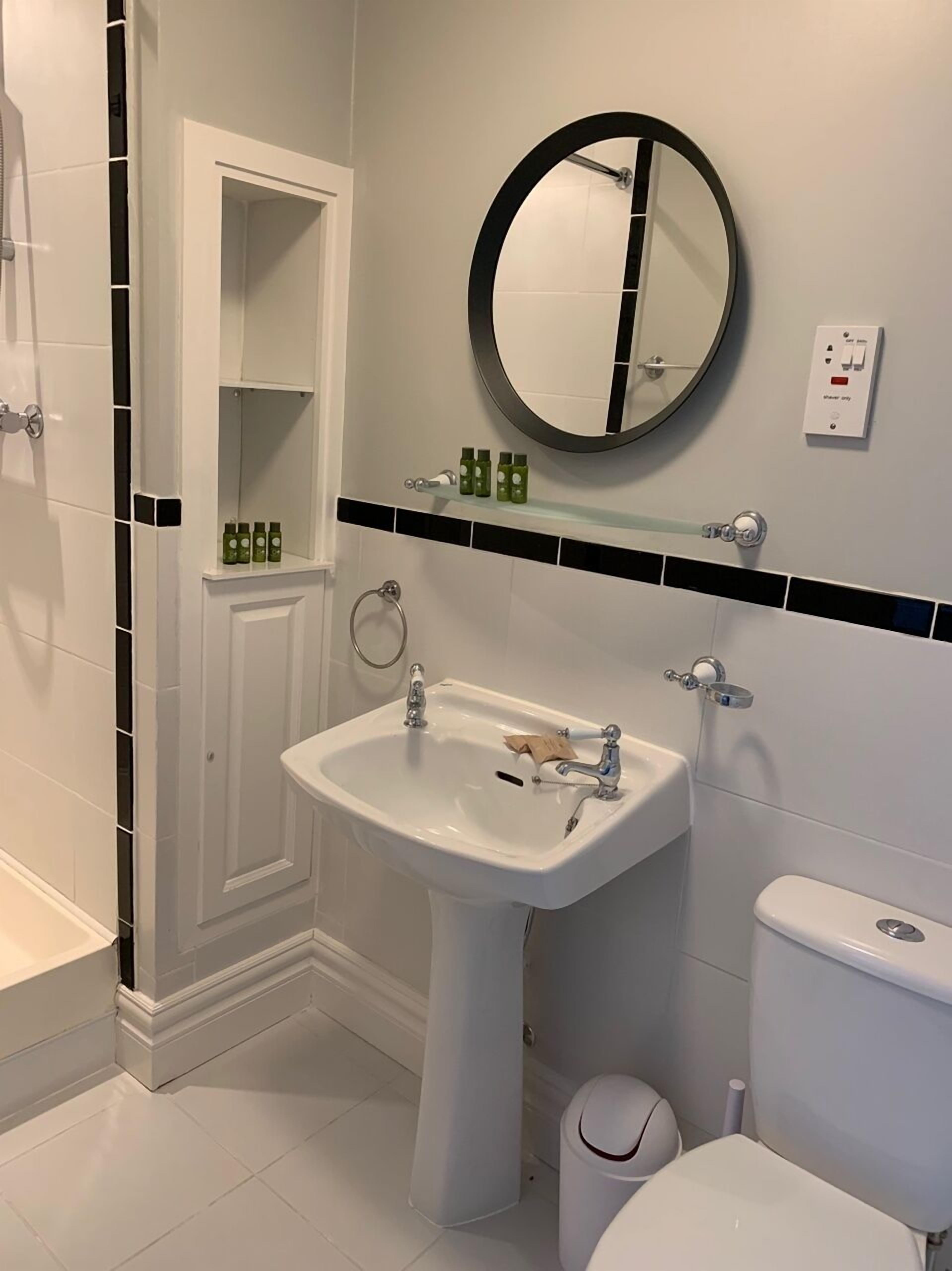 Une salle de bain avec un lavabo blanc, un miroir, des toilettes et un espace douche.