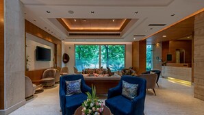 A spacious lobby with a large seating area, a reception desk, and a view of greenery outside. - Hotel Saket 27 (New Delhi)