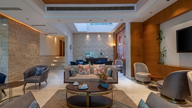 A spacious lobby with a high ceiling, a central seating area with sofas and armchairs, a coffee table, and a staircase leading to an upper level. - Hotel Saket 27 (New Delhi)
