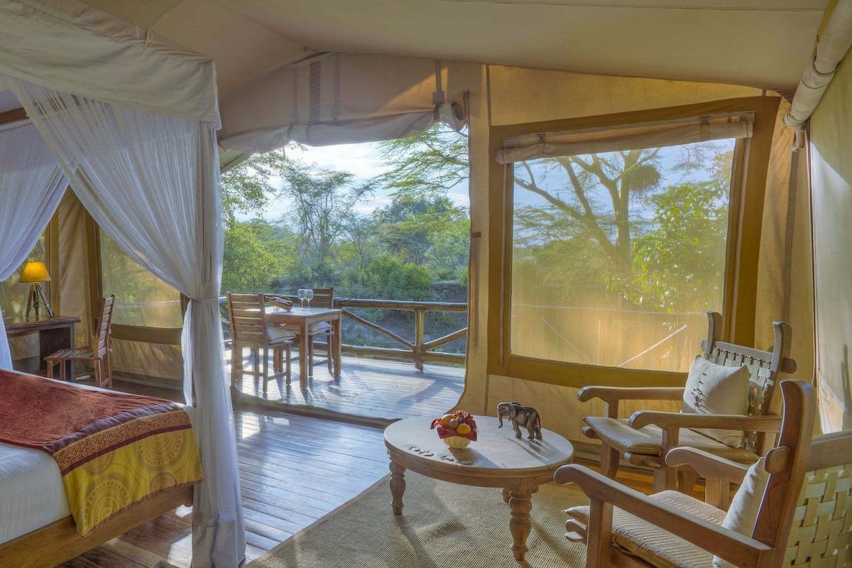 Un dormitorio con cama, mesita de noche, una silla y ventana con vista a árboles.