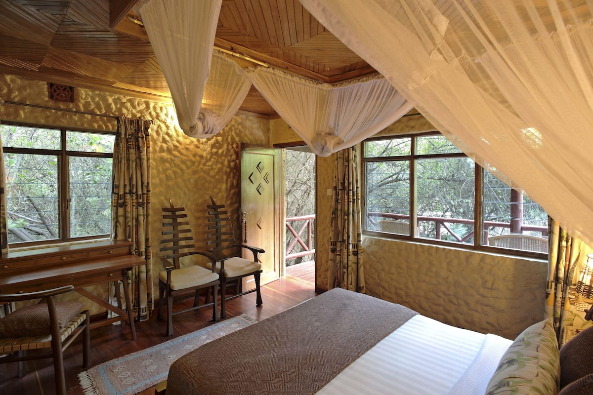 Un dormitorio con una cama grande, muebles de madera y ventanas con vistas a árboles.