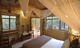 A bedroom with a large bed, wooden furniture, and windows with a view of trees.