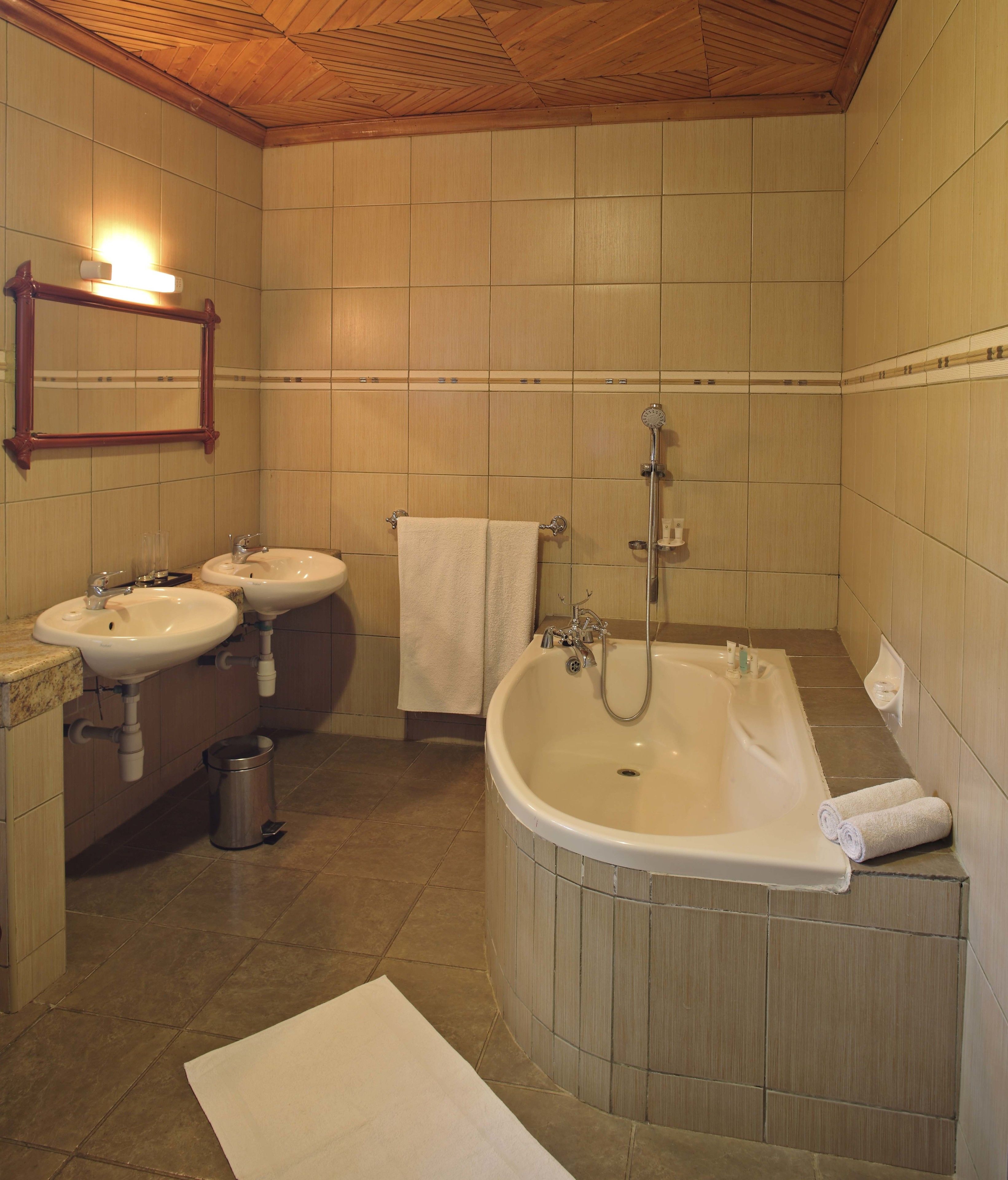 A bathroom with two sinks, a bathtub, a shower, and a wooden ceiling.