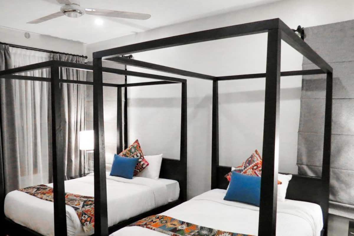 Una habitación con dos camas, cada una con estructura negra y ropa de cama blanca, y un ventilador de techo.