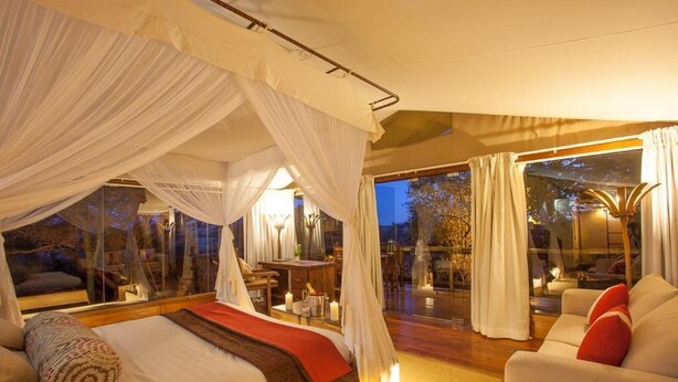 A bedroom with a canopy bed, a sofa, and a view of the outdoors. - Mara Leisure Camp (Maasai Mara)