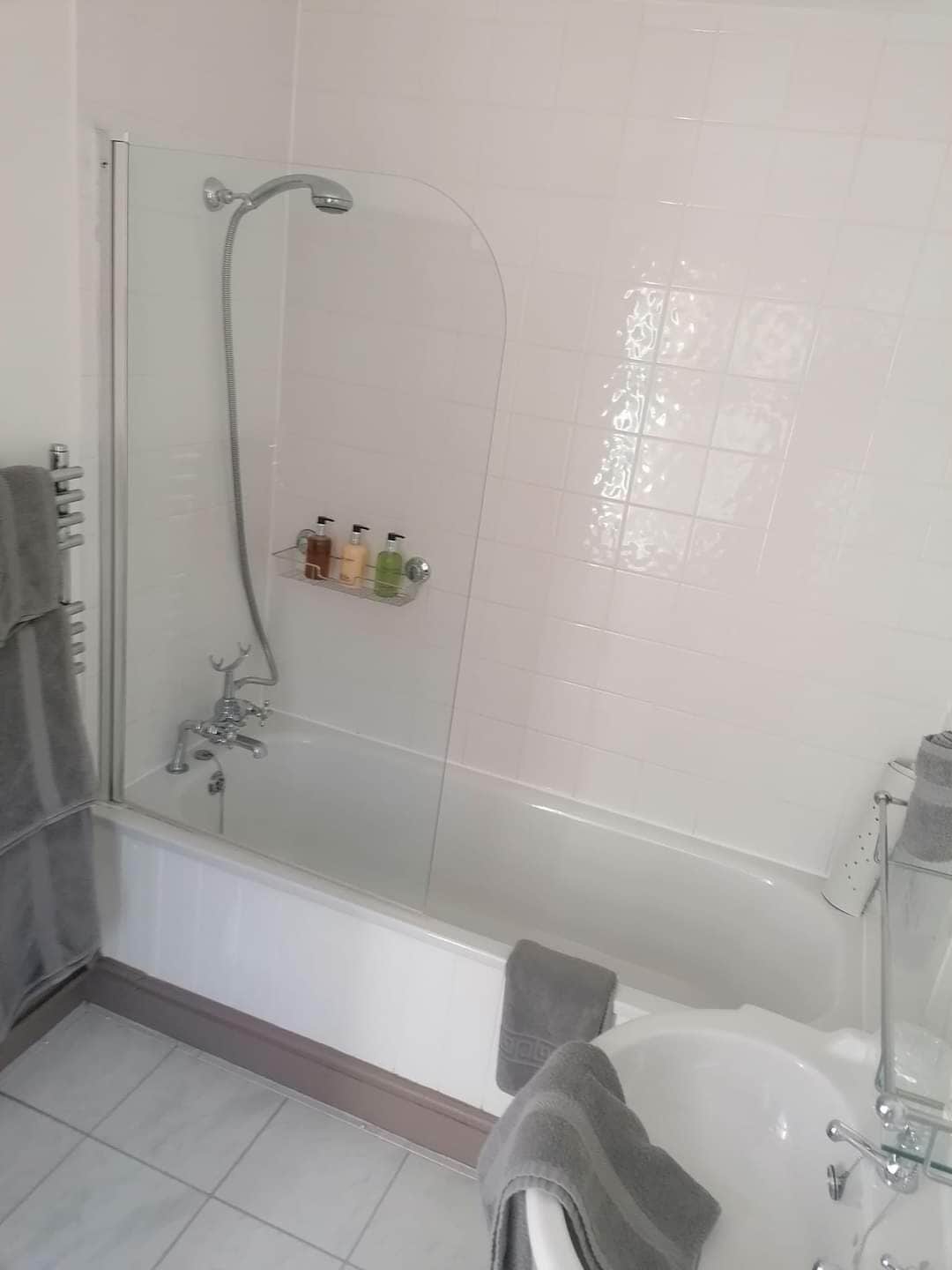 A bathroom with a glass-enclosed shower, a bathtub, and a shelf with toiletries.