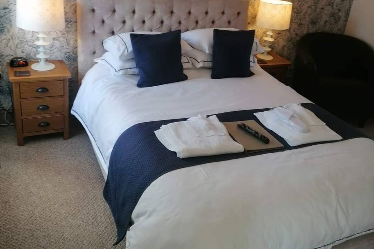 A neatly made bed with a tufted headboard, two bedside lamps, a nightstand with a phone, and a folded towel on the bed.