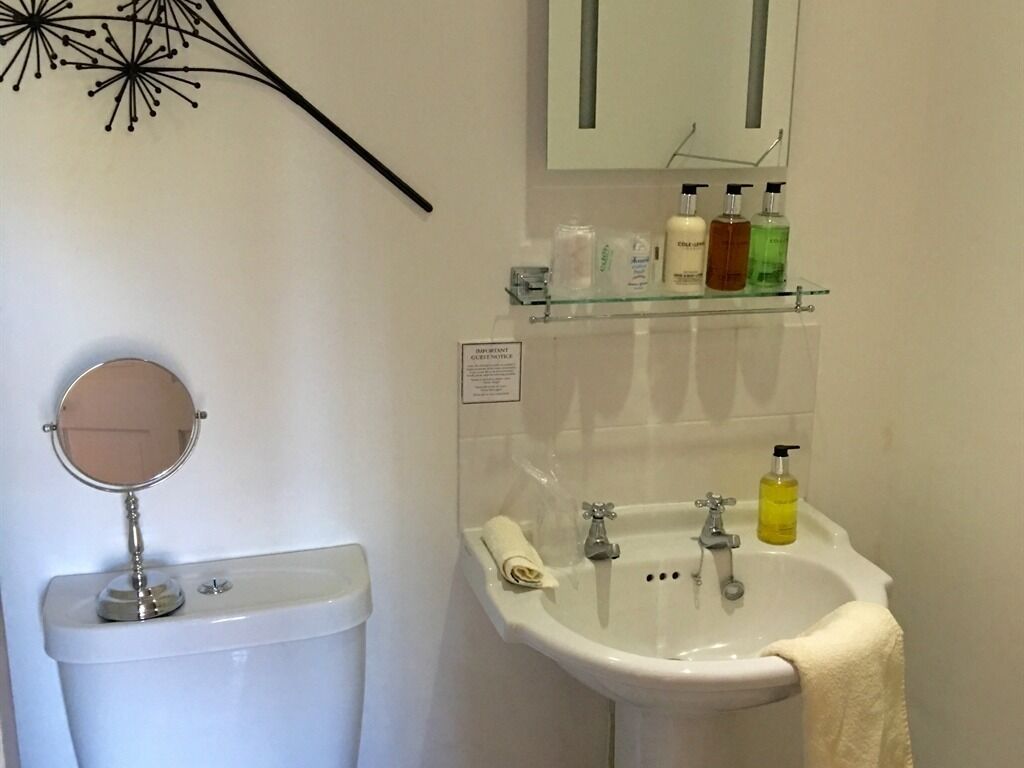 A bathroom with a toilet, a sink, and a mirror. There are toiletries on the sink and a towel hanging on the wall.