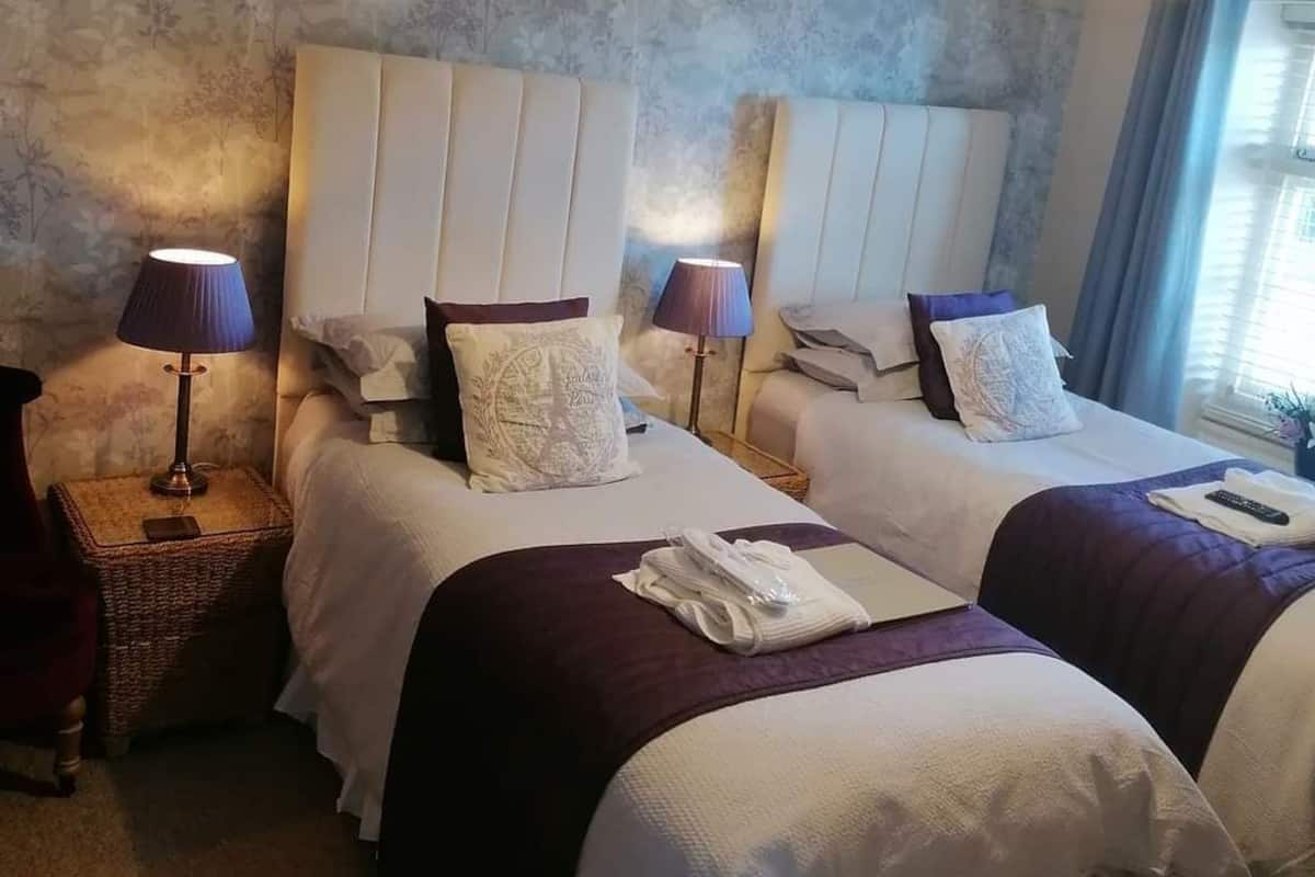 A hotel room with two beds, each with a headboard, bedside tables, lamps, and towels.