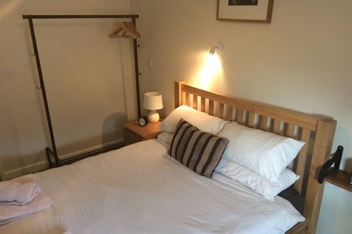 Una cama bien hecha con almohadas, una lámpara de noche y un cabecero de madera.