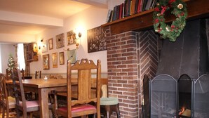 A cozy dining area with a brick fireplace, wooden furniture, and a Christmas wreath. - The Sun Inn (Ellesmere)