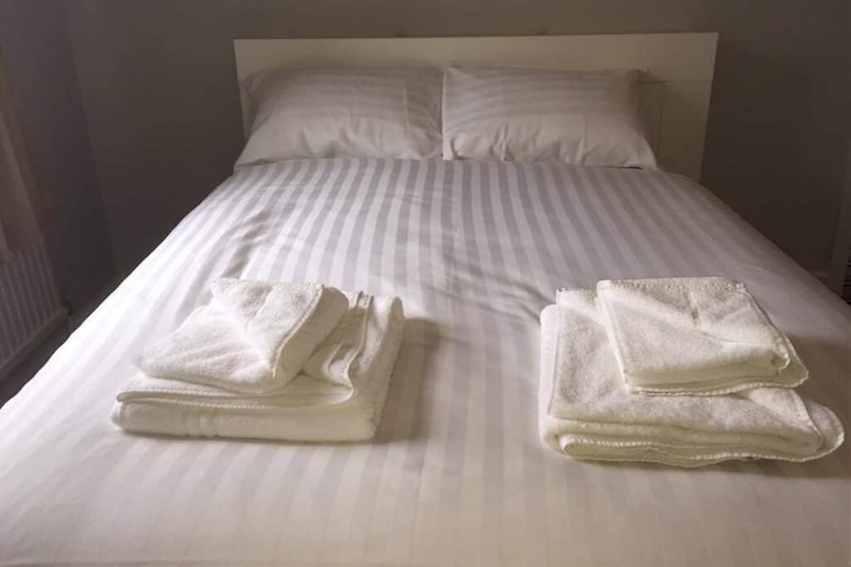 Uma cama bem arrumada com lençóis brancos e duas toalhas dobradas ao lado.