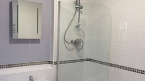 Ein Badezimmer mit einer Dusche in Glasabtrennung, einem Waschbecken und einem Spiegel an der Wand.