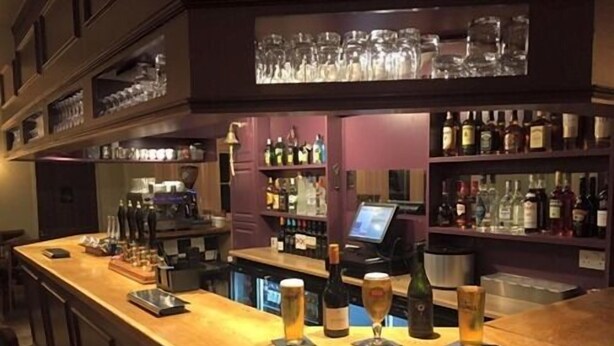 Eine Bar mit einer Holztheke, Barhocker und Regalen voller Flaschen.
