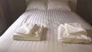 Ein ordentlich bezogenes Bett mit gestreifter Bettwäsche und zwei gefalteten Handtüchern auf der Seite.