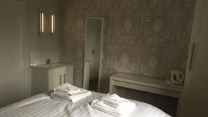 Ein Hotelzimmer mit Bett, Nachttisch, Spiegel, Waschbecken und einer Tür.