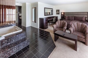 A modern hotel room with a large bed, a desk, a chair, a coffee table, and a bathroom with a bathtub and vanity. - Hôtel Motel Le Gite (Québec City)