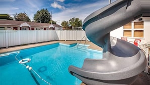 Una piscina con tobogán, una cuerda de seguridad y una valla blanca al fondo.