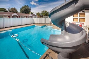 A swimming pool with a slide, a rope safety line, and a white fence in the background.