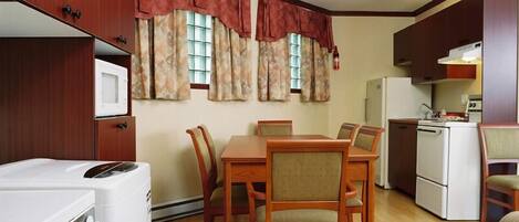 A compact kitchen with wooden cabinets, a dining table with chairs, and a refrigerator.