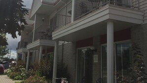 Un edificio de varios pisos con balcones, fachada de ladrillo y un camino pavimentado con plantas.